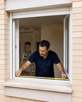 Instalador midiendo una ventana de PVC con cajón de persiana, visto desde la fachada